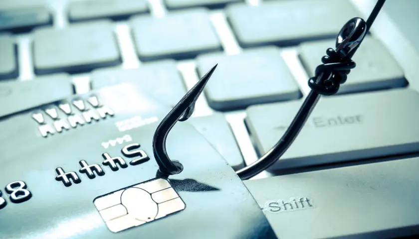 credit card phishing – piles of credit cards with a fish hook on computer keyboard